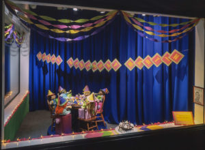 Large corner display window featuring cabbage patch kids of different races having birthday party, sitting around a small table with cake, birthday colorful hats, and noisemakers.