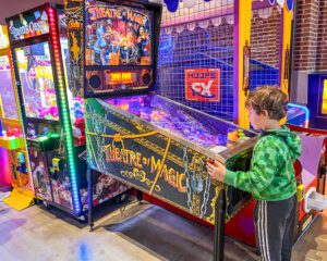 A little boy playing a pinball game called Theater of Magic